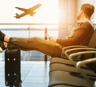 man sitting on gang chair with feet on luggage looking at airplane