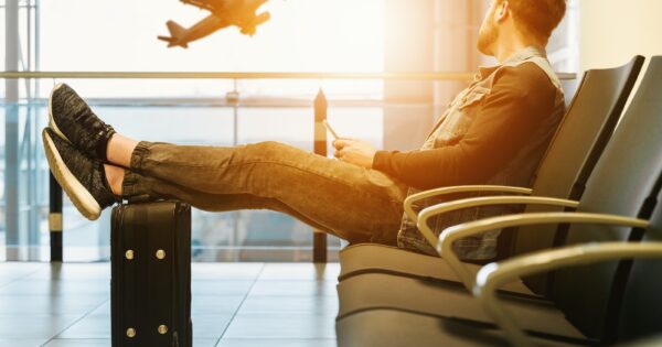 man sitting on gang chair with feet on luggage looking at airplane